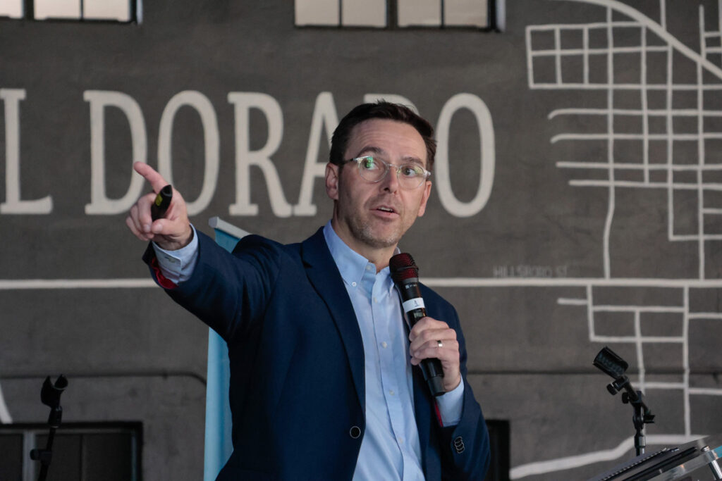 A regional meeting speaker gestures to a presentation screen.