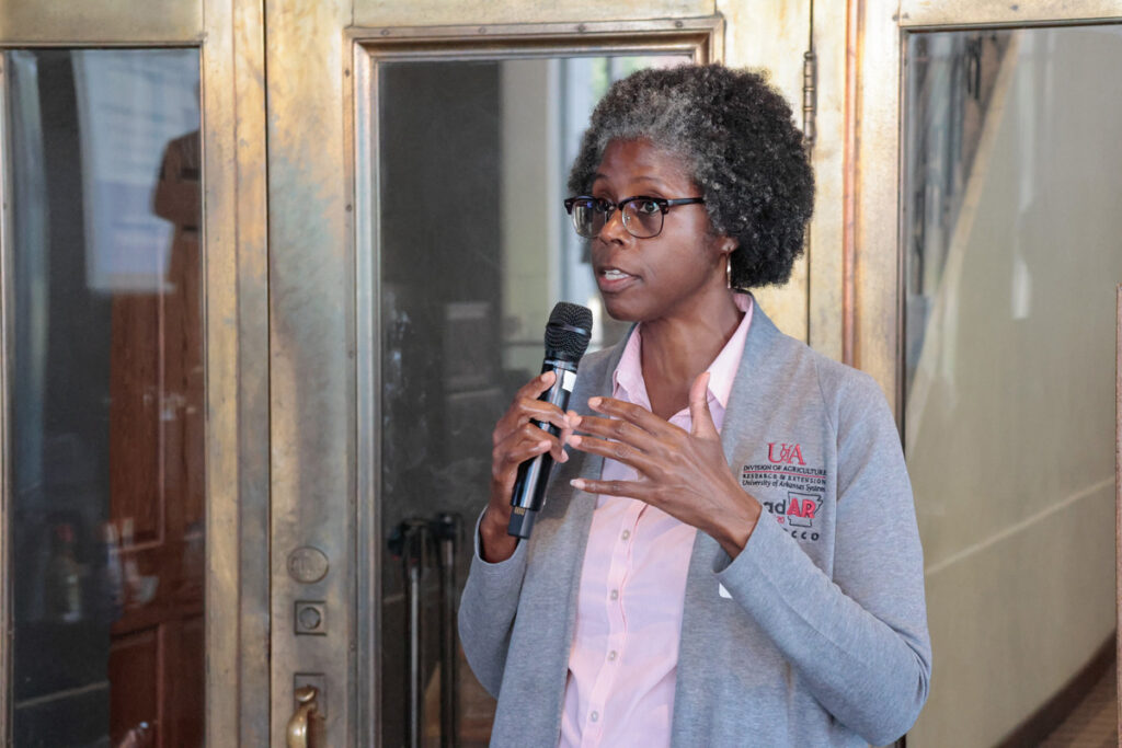 A Black woman in a gray U of A cardigan and pink blouse holds a microphone and asks a question during a regional meeting panel discussion.