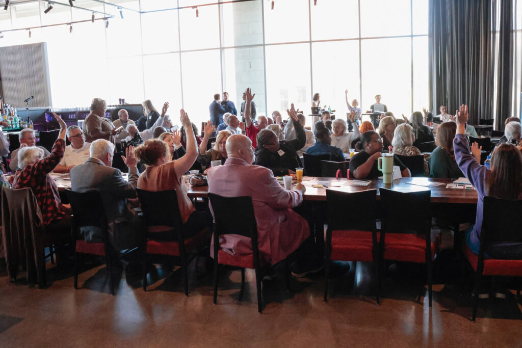 A group of regional meeting attendees in El Dorado raise their hands in response to a question from moderators.